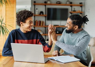 Adult and teen working at laptop, smiling and highfiving