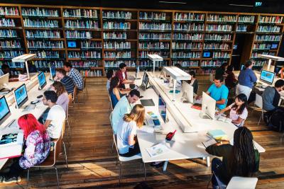 Teens sitting at a table with computers in a library