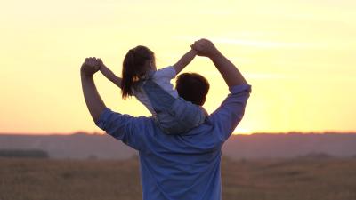 child sits on father's neck waving his arms together flying like an airplane