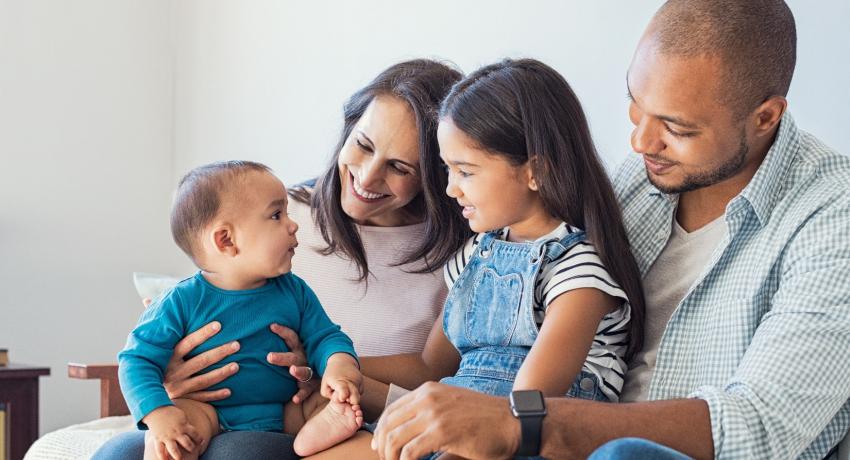 Multiracial family sits closely together on a sofa and smiles. 