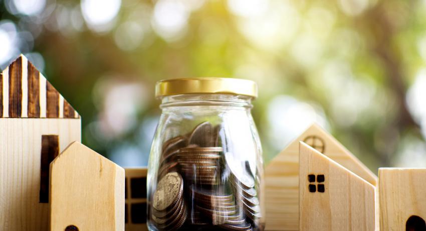 Toy blocks arranged into houses alongside a jar of quarters. 