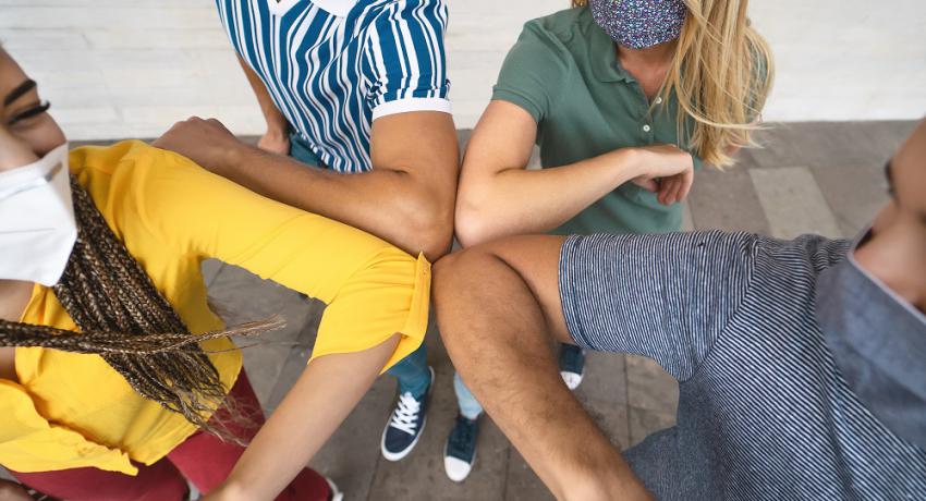 Young friends wearing face masks greet with elbows bumps for preventing corona virus spread.