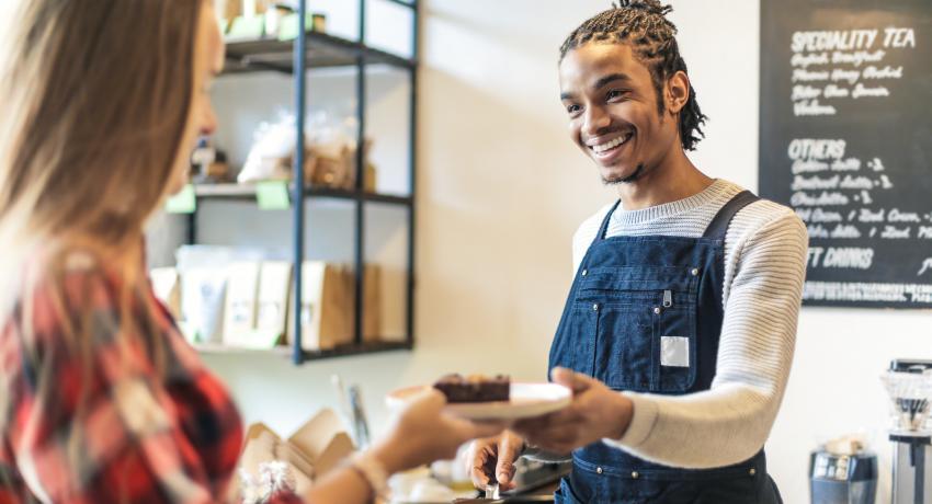 Male barista hands a customer a pastry.