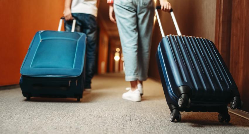 Two youth walking down a hotel hallway with suitcases. 