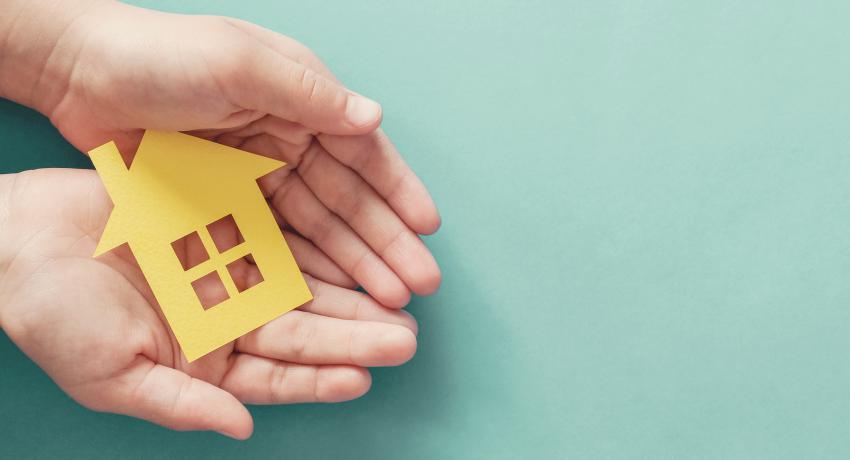 Child holds yellow paper house in their palms.