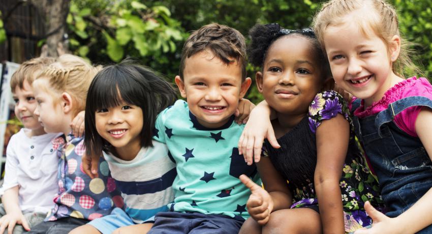 Children smiling outside with their arms around each other. 