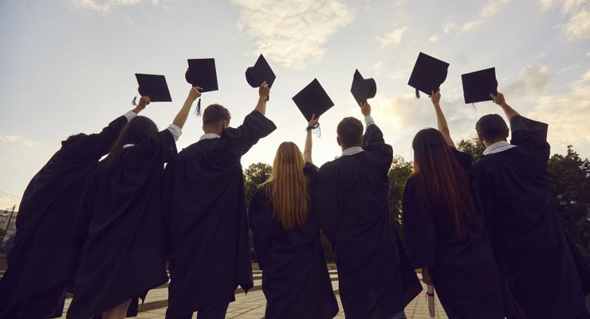 Youth hold their graduation caps in the air. 