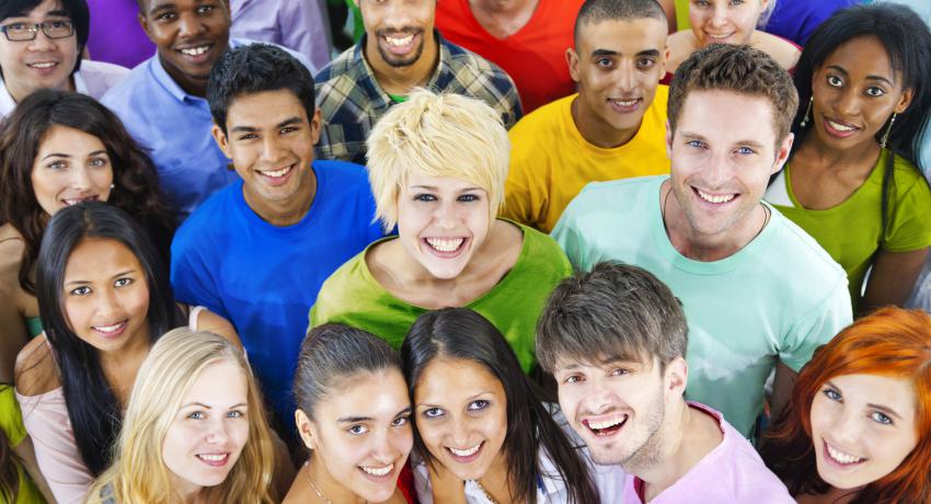 A large group of young adults stand together in colorful shirts smiling. 