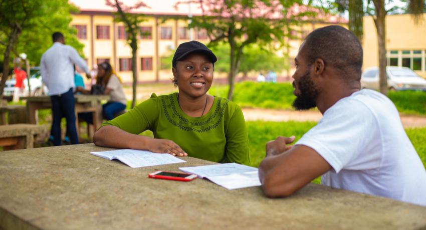 Mentor sits with young adult going over homework in outdoor setting. 