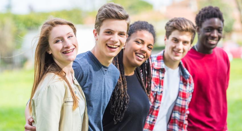 A group of smiling young people in a park setting. 