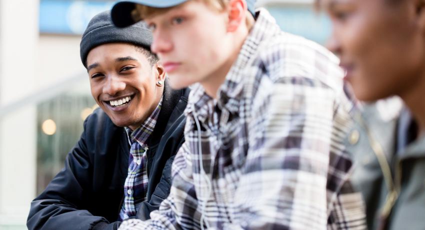 Three smiling youth hanging out on a bench. 