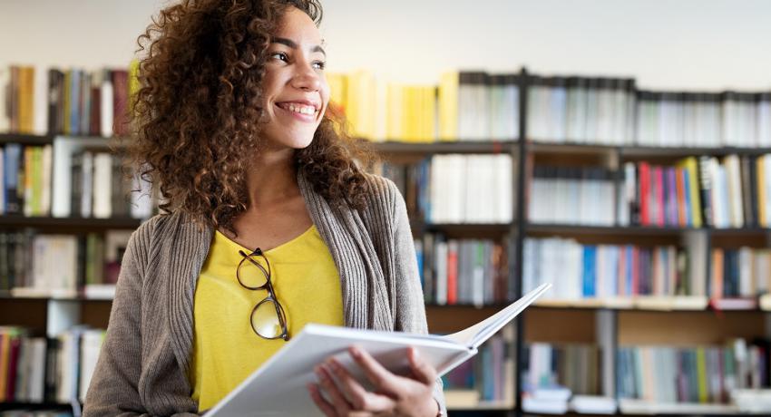 Smiling student reading book in library