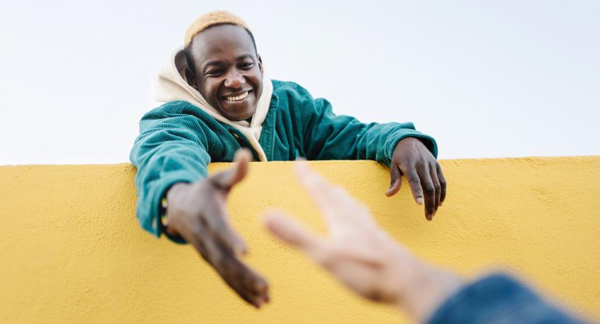 Young man extending a hand down to help another person over a wall