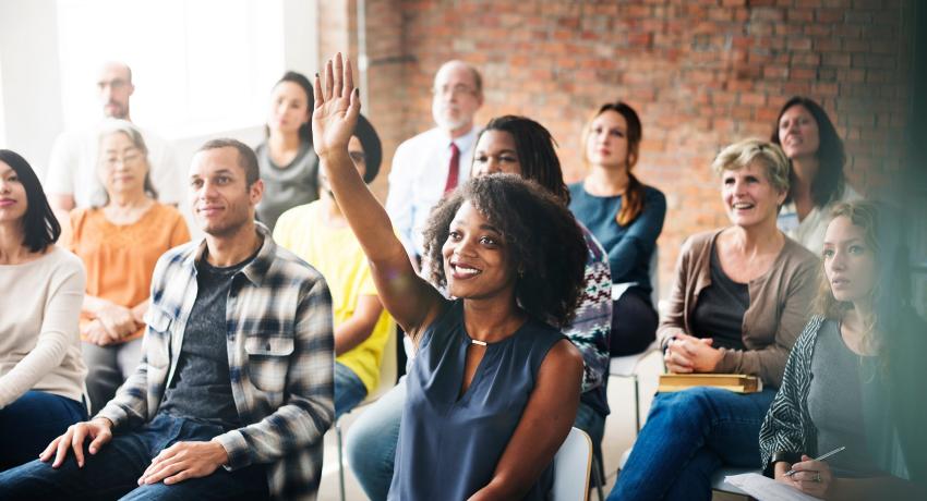 group of people sitting in chairs woman smiling raising hand