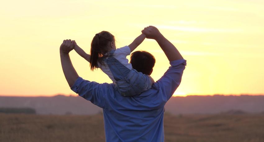 child sits on father's neck waving his arms together, flies like an airplane.